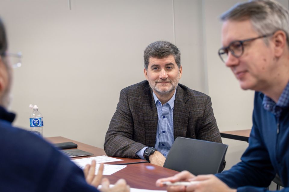 Leading Change from the Middle a man in the middle of two other people sits listening at a desk