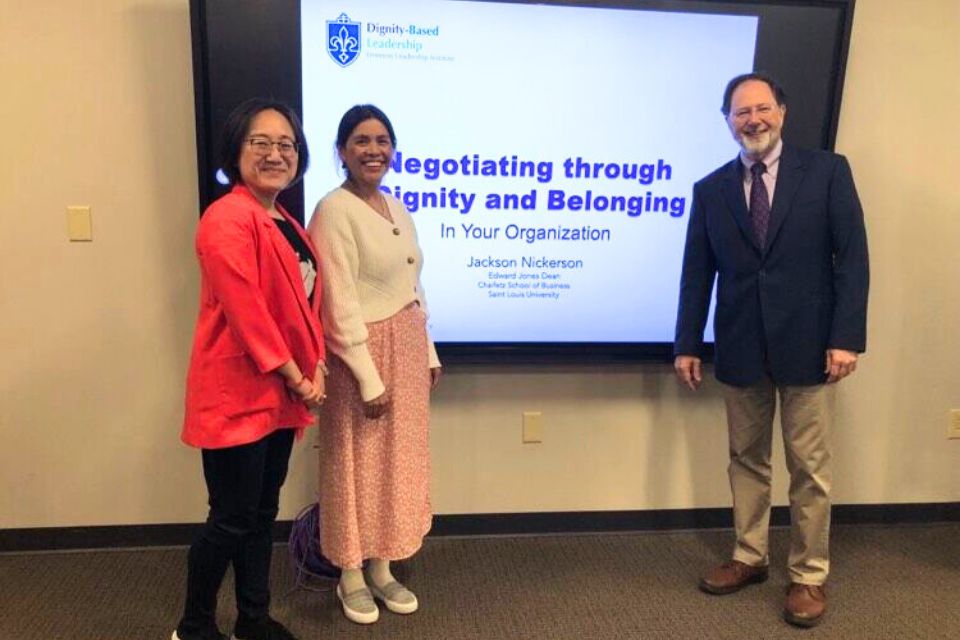 Negotiating Through Dignity and Belonging three people stand posed for a photo in front of a screen