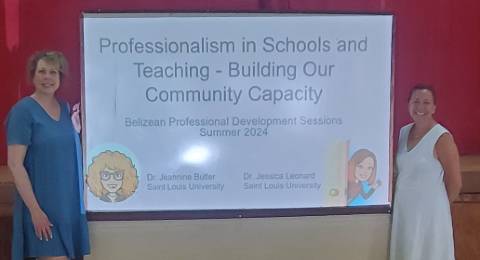 Two professors stand on either side of a video screen that reads "Professionalism in Schools and Teaching: Building Our Community Capacity. Belizean Professional Development Sessions June 2024"