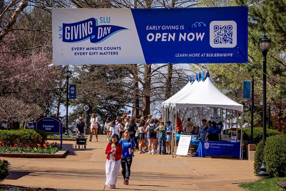 People walk under a banner on campus that says SLU Giving Day.