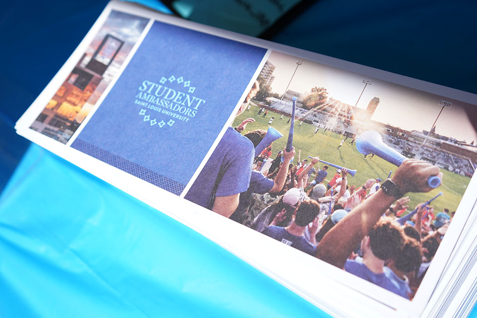 A brochure on a table has a photo of students cheering and says student ambassadors.