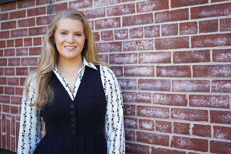 A student poses for a photo near a brick wall.