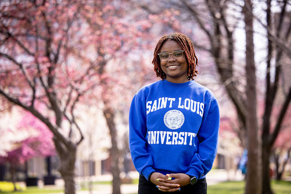 Malaisyah Vann poses for a photo outside on campus with pink flowering trees behind her. 