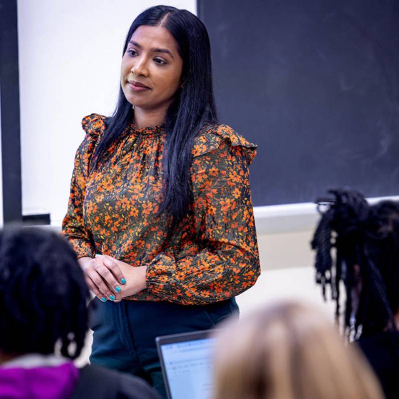 A professor talks to students at the front of a classroom.