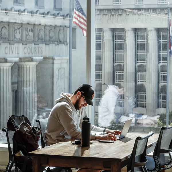 A male student studies at a desk in the SLU School of Law. The front of the St. Louis Civil Courts Building can be seen behind him through the window.