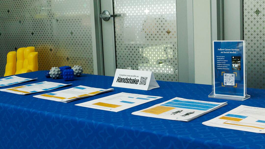 A table with Career Services handouts, including a sign asking whether the student completed their Handshake profile.