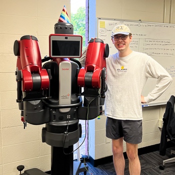 Pascal Sikorski staning next to and smiling with a robot in the Mecharithm Lab.