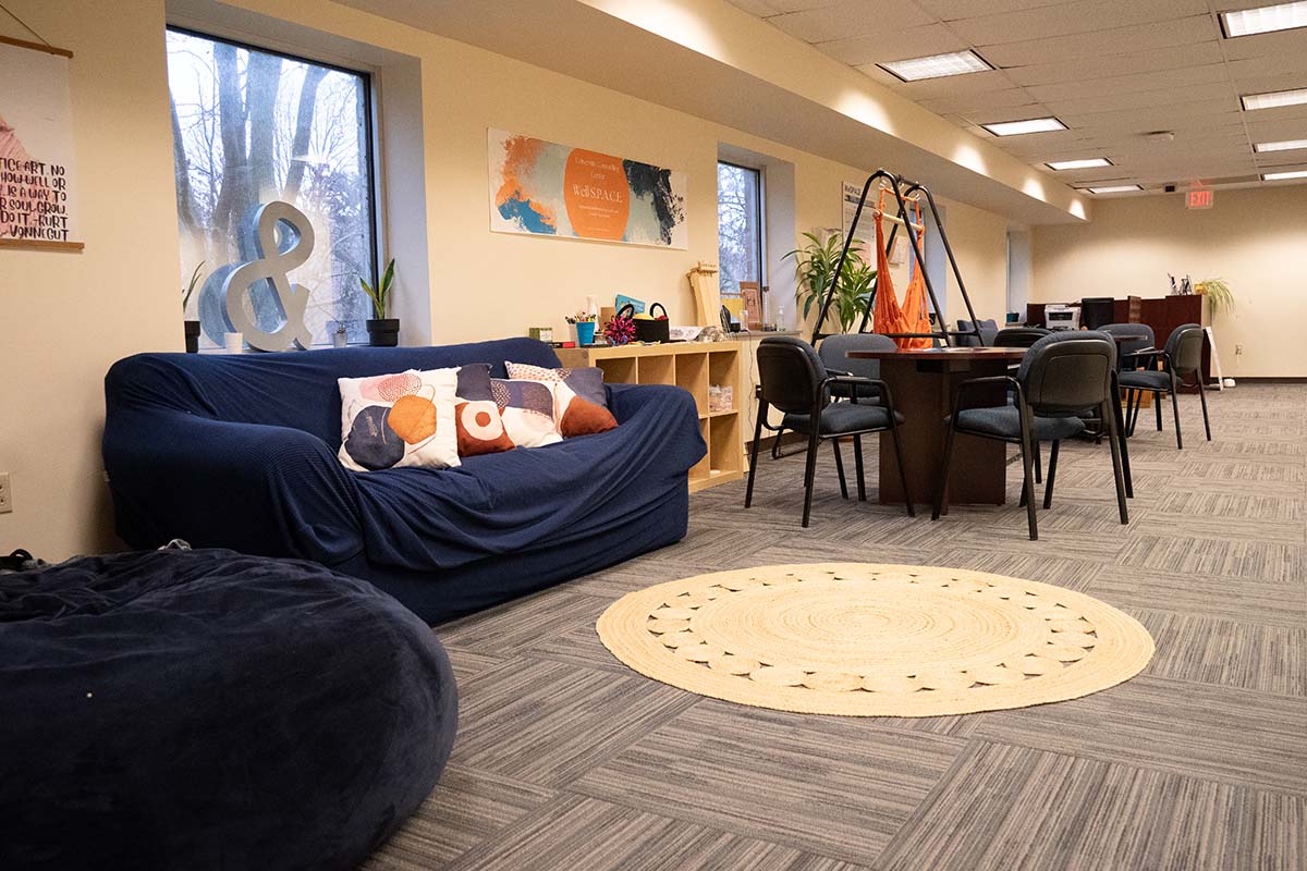 Image of a room with carpeting, a round area rug, a comfy looking couch, bean bag chair, and tables with chairs.