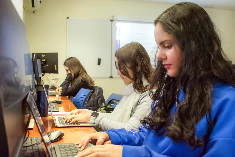 Three students studyng with their laptops in class.