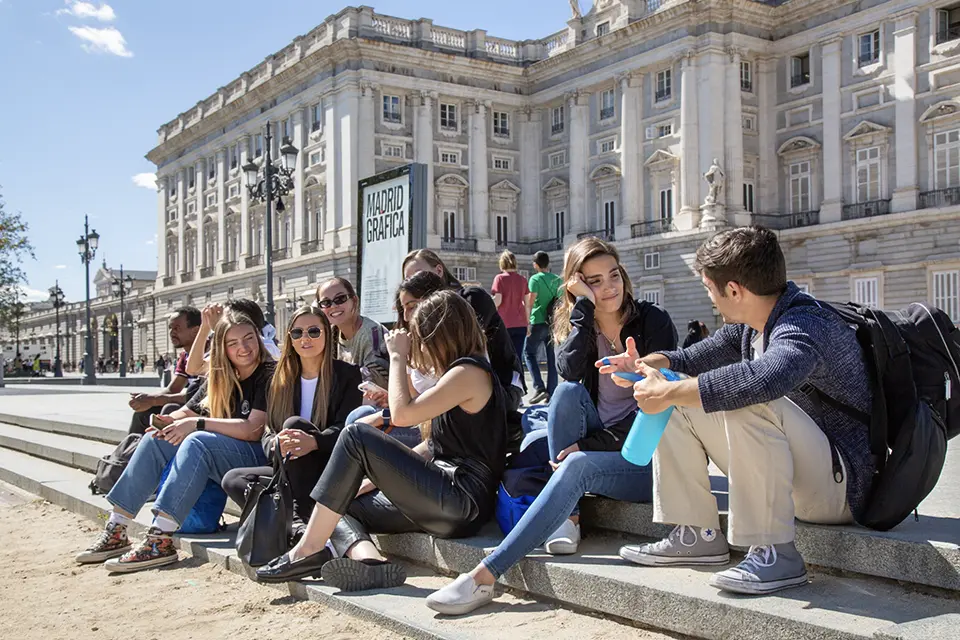 Students sit on steps outside a large white building with columns.