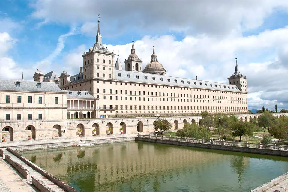 Exterior shot of a monastery with a large pond in the patio.