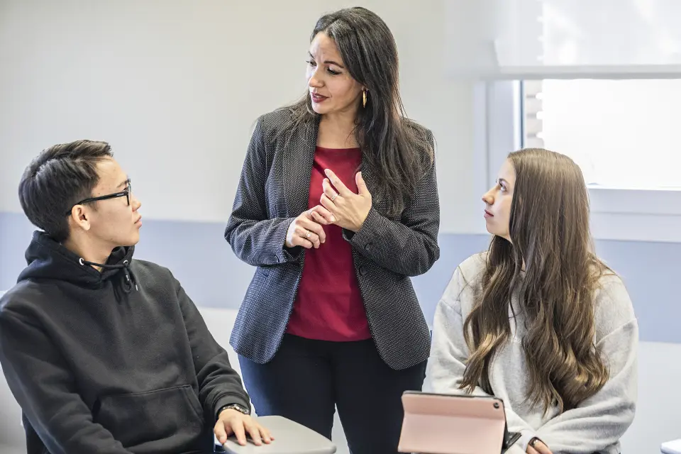 Two students in class talking with the professor.