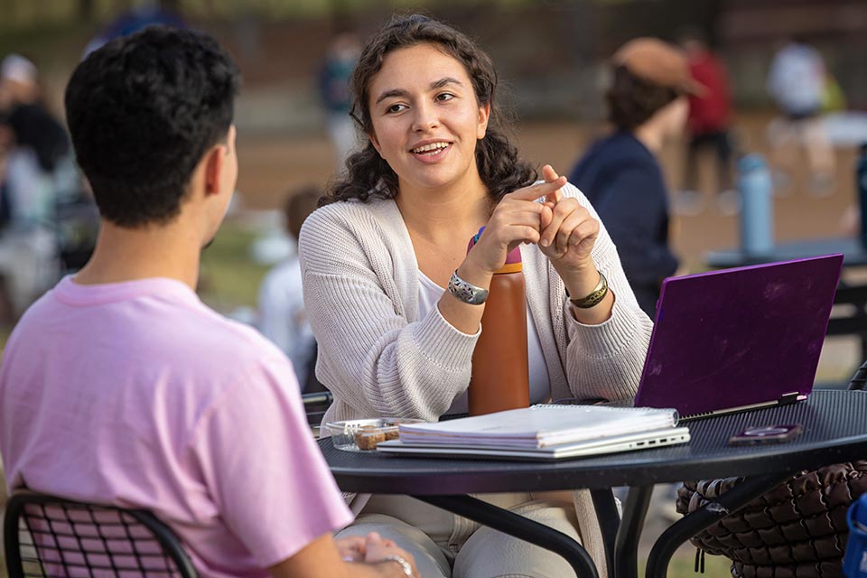 Students with laptop at table outdoors
