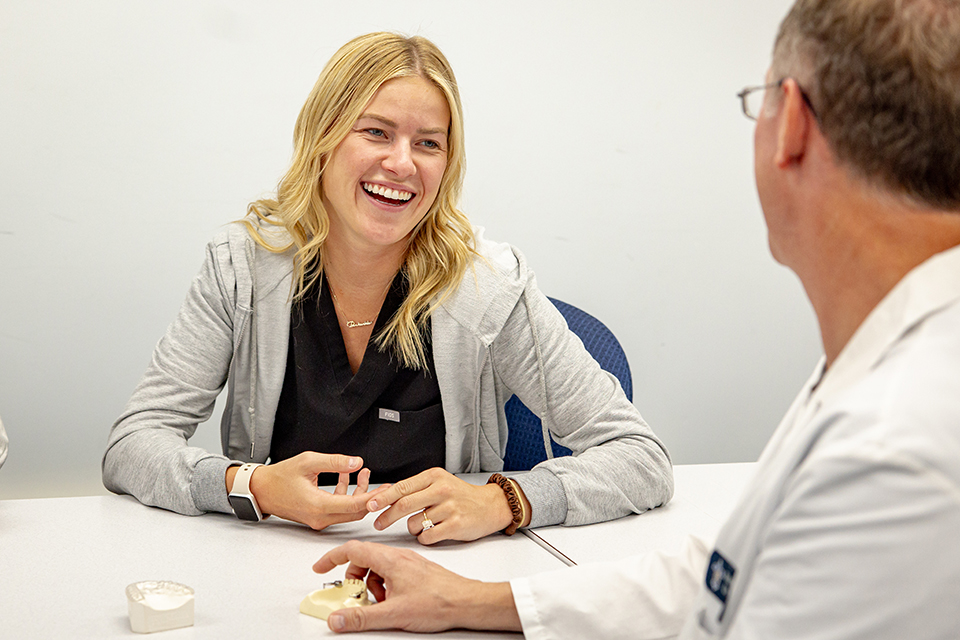 Daniel C. Stoeckel, D.D.S. right, works with a resident during a class. They sit across from each other at a table. The resident is laughing.