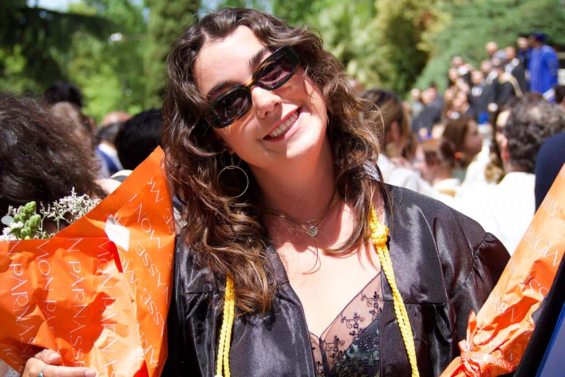 A photo of Quinn Riordan in her graduation robe and holding a bouquet of flowers at the SLU-Madrid Commencement. 