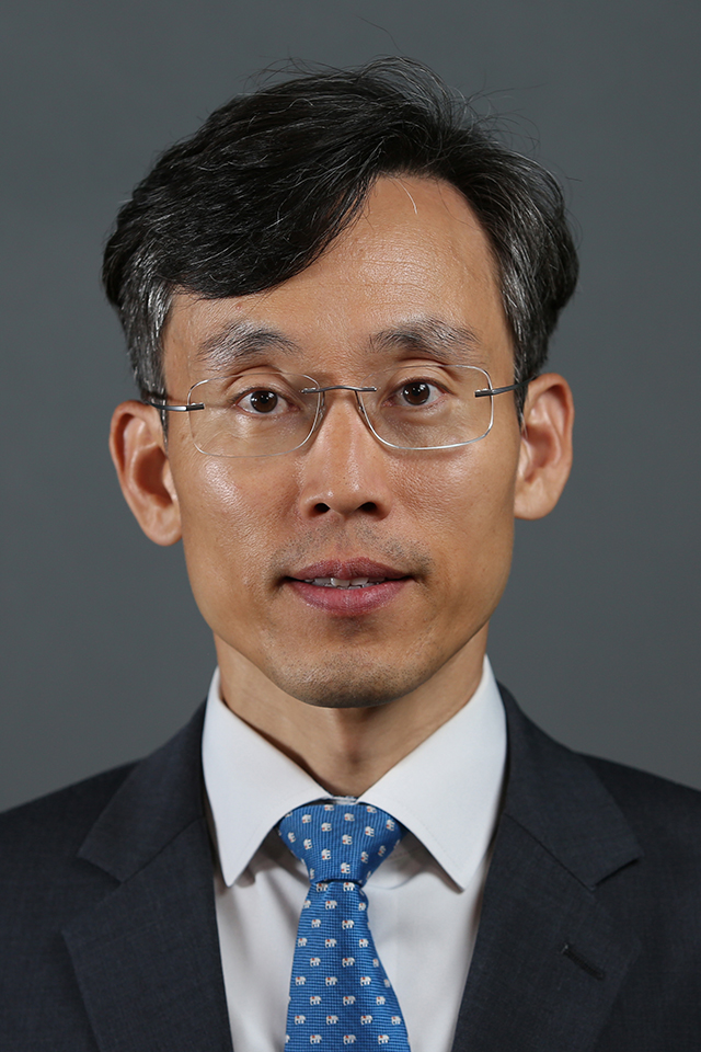 A headshot of SangNam Ahn, Ph.D. He smiles for a photo against a gray background.