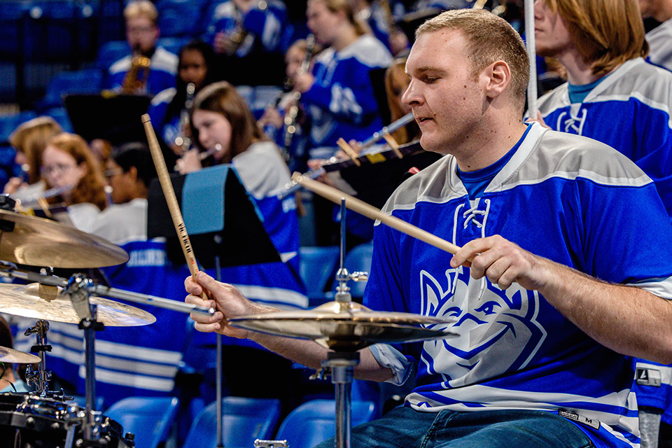 Billiken Pep Band drummer A blonde man in a blue-and-white hockey jersey drums.