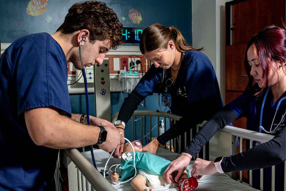 Three nursing students treat a simulated infant patient in a SLU nursing lab.