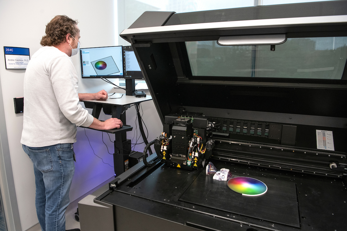 Individual stands at a computer next to a 3D printer