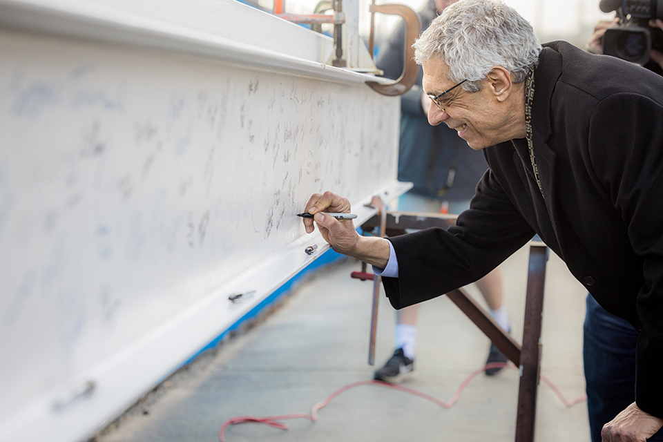 Pestello signs a large white beam with a Sharpie during construction of the O’Loughlin Family Champions Center.