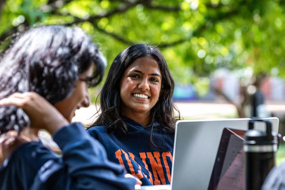 Two women smiling while taking a break outside at table with laptop